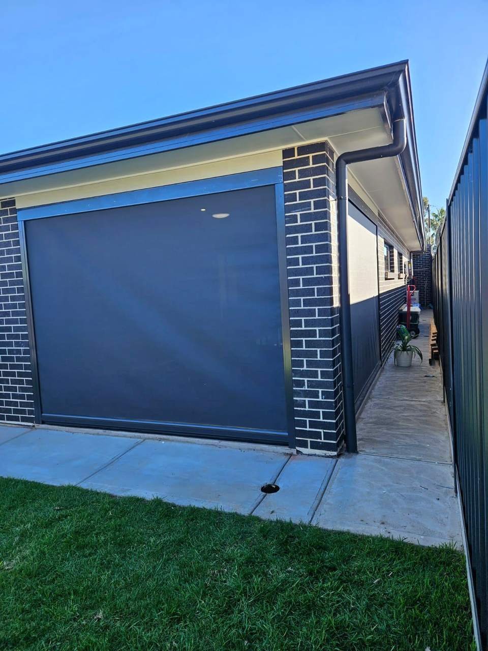Charcoal zip-track outdoor blind lowered on a brick patio