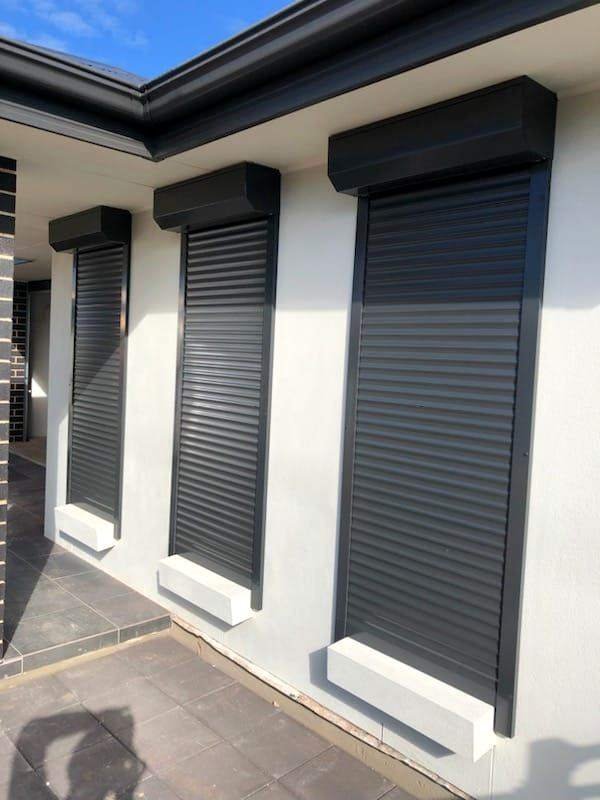 Charcoal aluminium roller shutters on three windows of a rendered home